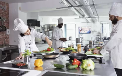 Chefs preparando alimentos em cozinha industrial moderna equipada com lavadora de xícaras e copos profissional.