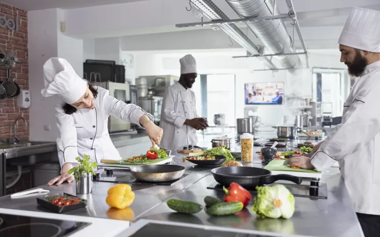 Chefs preparando alimentos em cozinha industrial moderna equipada com lavadora de xícaras e copos profissional.