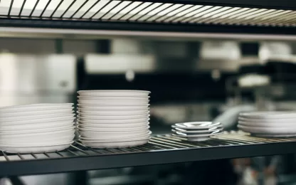 Prateleira de cozinha profissional com pilhas de pratos limpos, indicando higienização feita com máquina de lavar louça industrial.